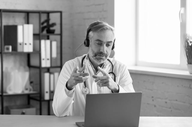 A physician at his desk reviewing a case on a laptop